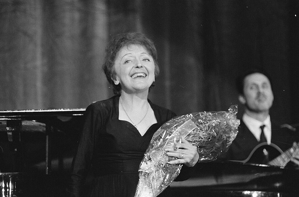 edith piaf con un ramo de flores en un escenario sonriendo